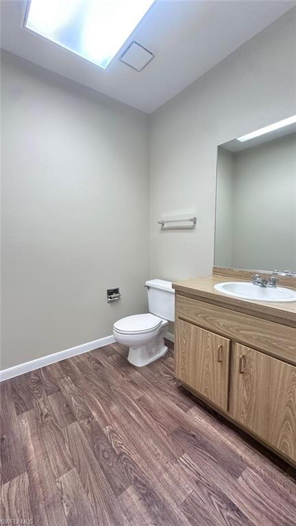 Bathroom featuring wood-finish flooring, a vanity with wood-finish cabinetry, an integrated sink, and a skylight