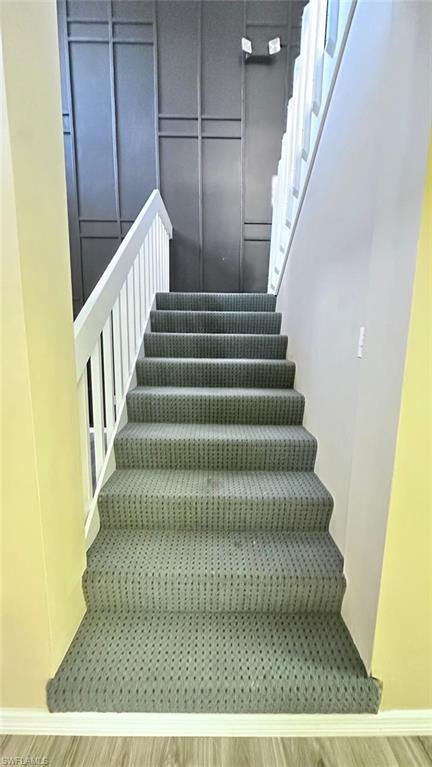 Staircase with patterned carpeting, white balusters, and a contemporary dark accent wall with geometric molding