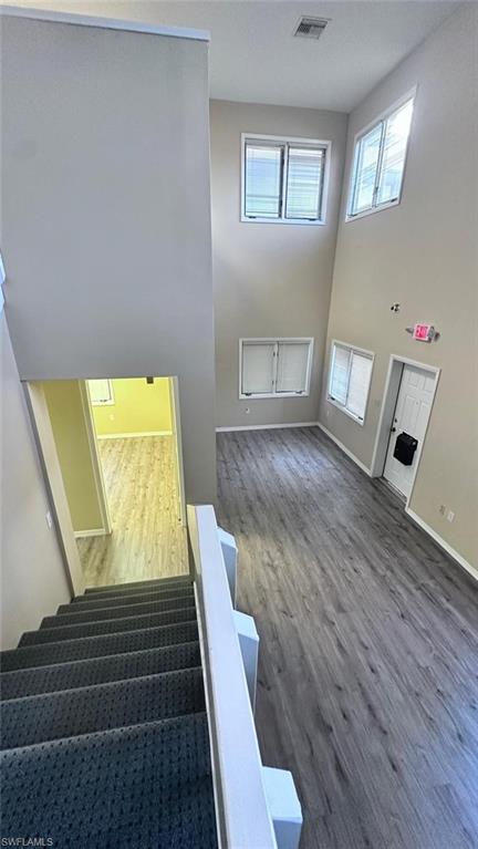 Open-concept living space featuring high ceilings, multiple windows, wood-finish flooring, and a carpeted staircase with a white railing