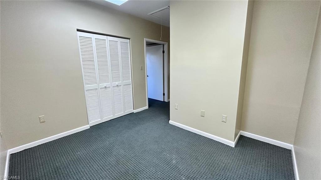 Interior room featuring neutral wall paint, white louvered bi-fold doors, dark patterned carpeting, and white baseboards
