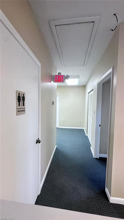 Hallway featuring dark patterned carpet flooring, light neutral-toned walls, and white trim