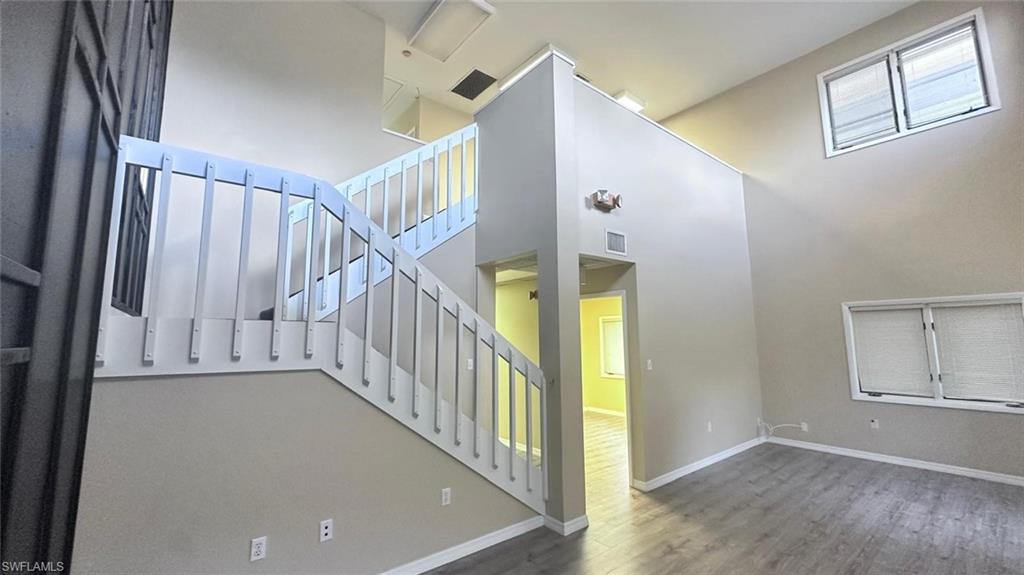 Interior staircase with white balusters and handrail, neutral wall tones, wood-finish flooring, and high ceilings