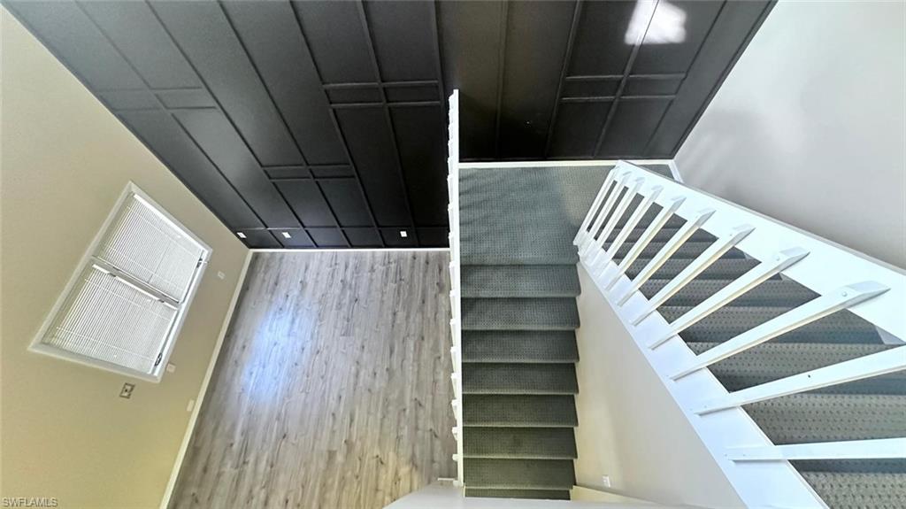 Entryway featuring a black coffered ceiling with recessed lighting, light wood-finish flooring, a window with blinds, and a staircase with white railings and carpeted treads