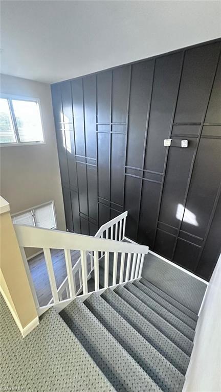 Staircase featuring light-colored carpeting, white balusters, and a decorative dark accent wall with horizontal and vertical trim