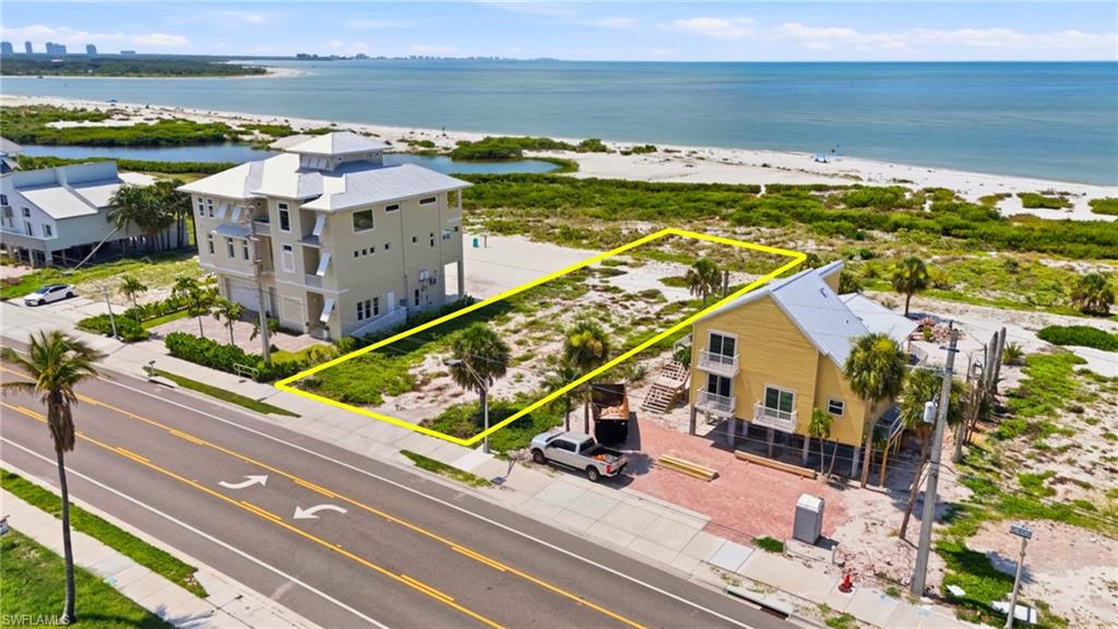 Expansive vacant lot featuring direct beachfront access with a sandy shoreline, a paved roadway frontage, and mature palm trees - Virtually Edited Image