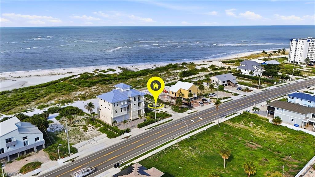 Elevated coastal home featuring multiple balconies, a light blue metal roof, and direct beach proximity - Virtually Edited Image