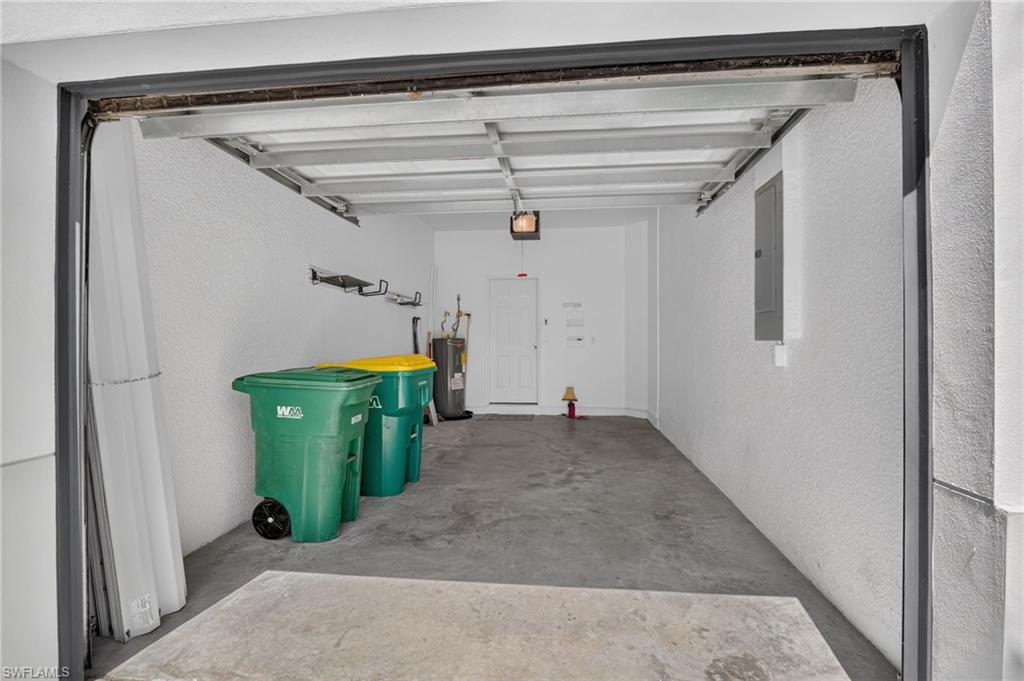 Concrete flooring garage with an overhead door, white textured walls, and built-in shelving
