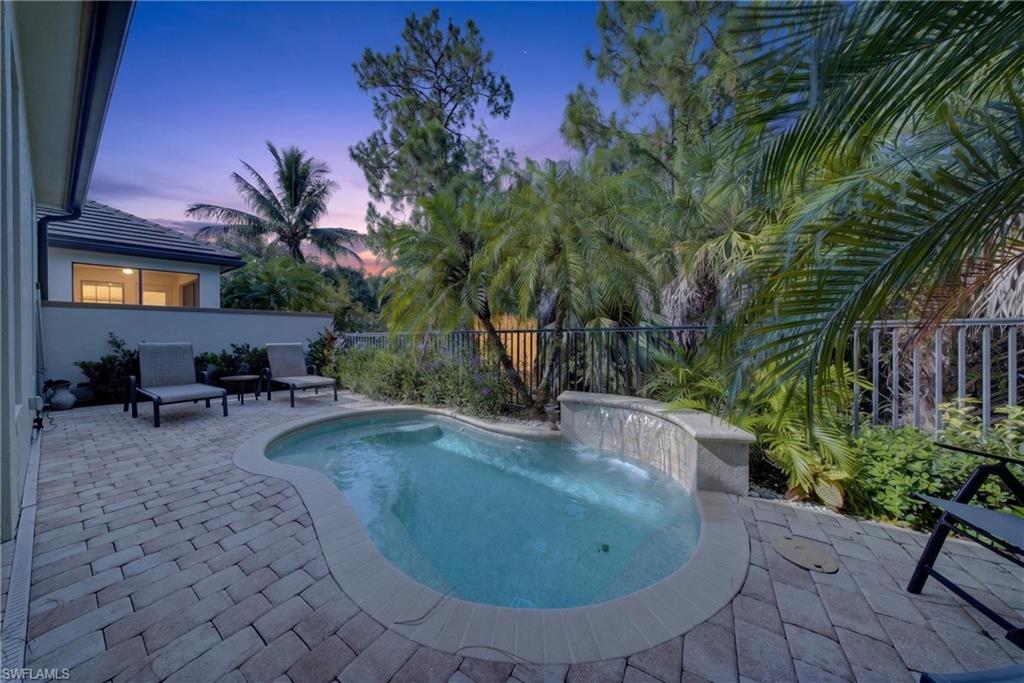 Outdoor patio featuring a freeform swimming pool with a waterfall element, surrounded by paver decking and lush tropical landscaping