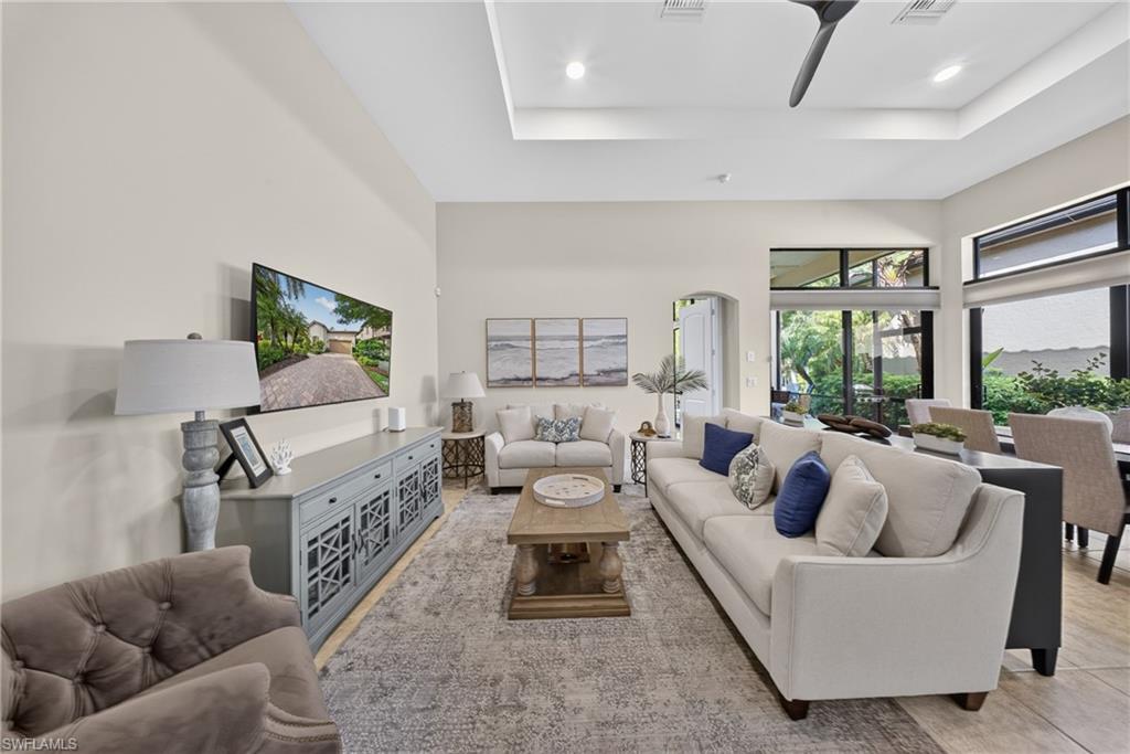 Spacious living area featuring a tray ceiling with recessed lighting, an integrated ceiling fan, and large windows with transom panels