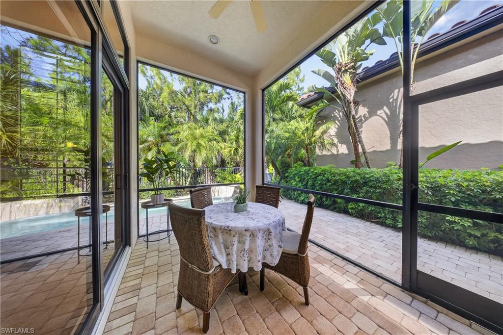 Screened lanai with herringbone paver flooring, overhead ceiling fan, sliding glass doors, and lush tropical landscaping