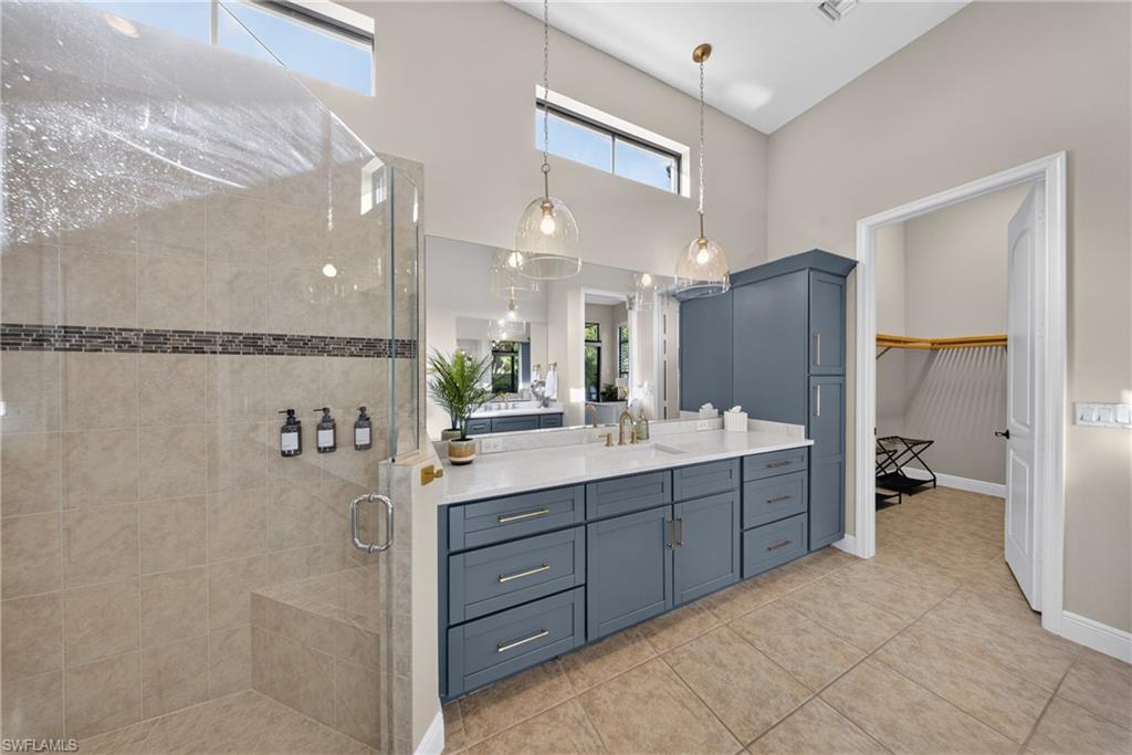 Spacious bathroom featuring a glass-enclosed shower with tiled bench, double vanity with quartz countertop, extensive blue cabinetry, and high ceilings with transom windows