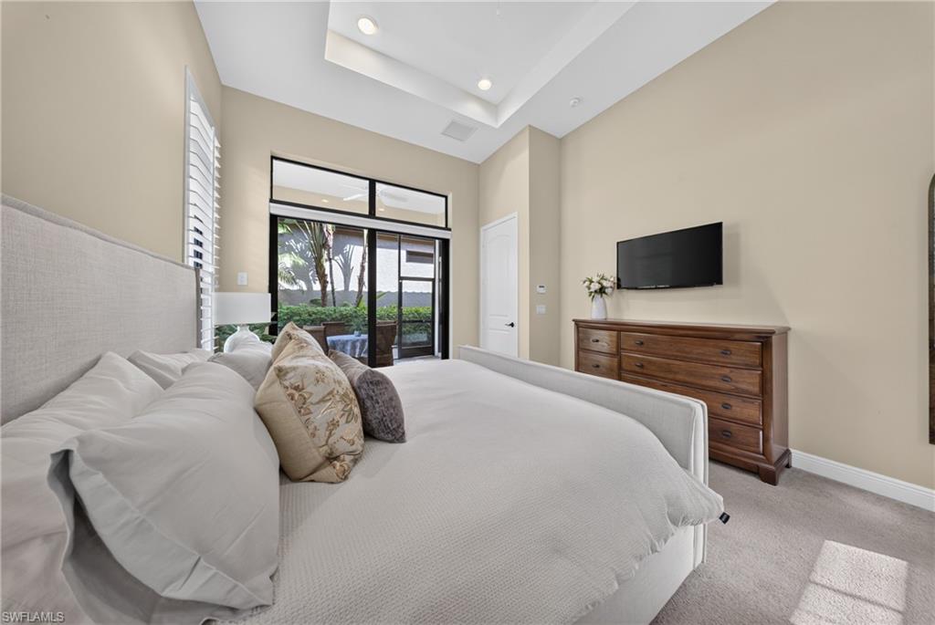 Spacious room featuring a tray ceiling, plantation shutters, and sliding glass doors with transom windows