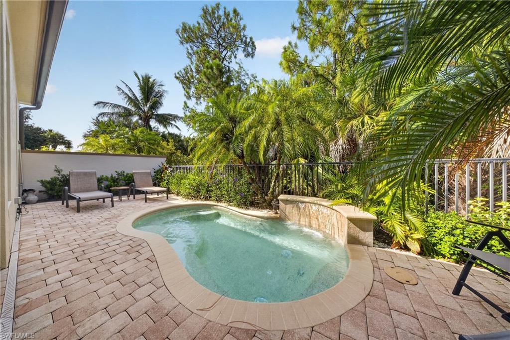 Pebbled pool with water feature, surrounded by paver patio and lush tropical landscaping