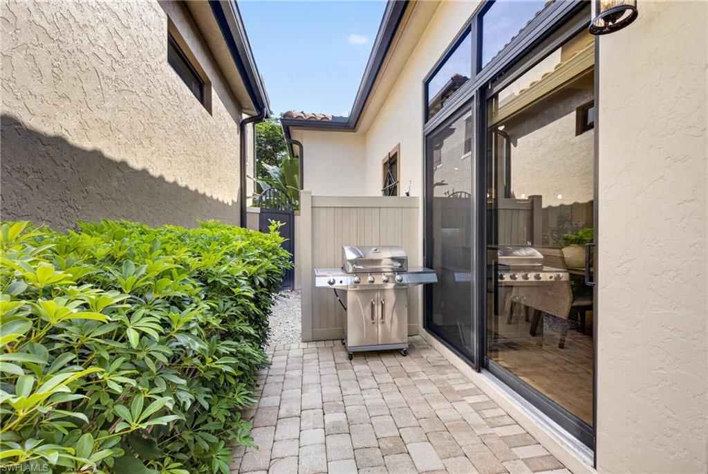 Paver patio featuring a privacy fence, established shrubbery, sliding glass door, and exterior sconce lighting