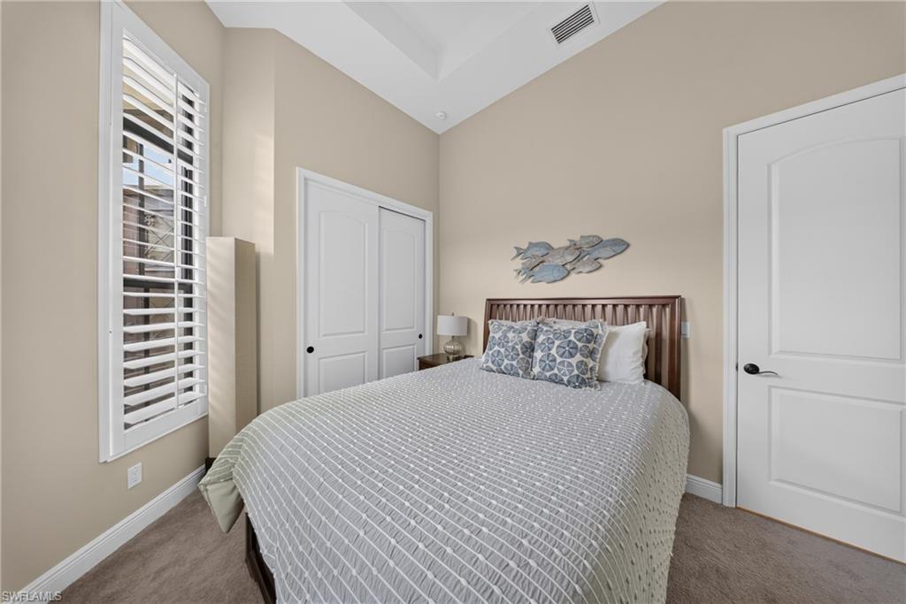 Carpeted bedroom featuring a vaulted ceiling and a tall window with plantation shutters