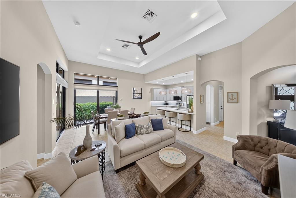 Open-concept living area featuring a tray ceiling with recessed lighting and a ceiling fan, tile flooring, and arched doorways