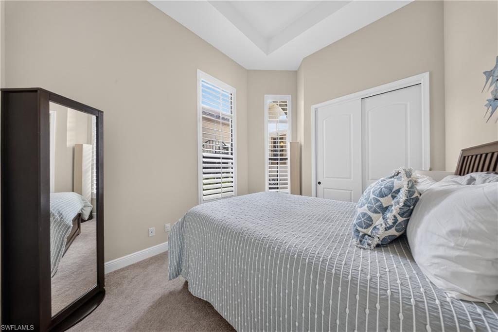 Tray ceiling room with neutral-toned walls, two windows featuring plantation shutters, and carpet flooring