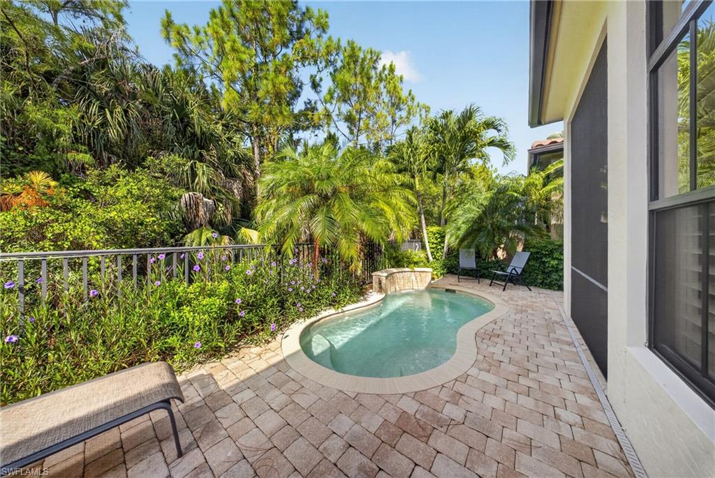 Pebbled pool with a built-in spa and waterfall feature, surrounded by paver decking and mature tropical landscaping