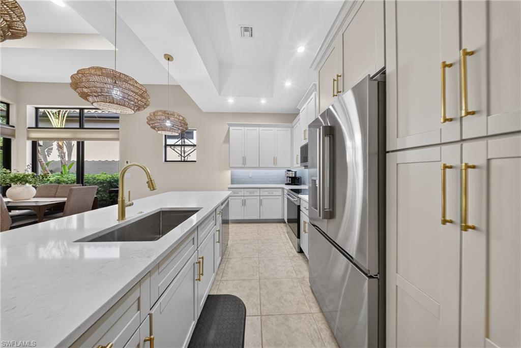 Modern kitchen featuring a large island with an undermount sink and gold-finish faucet, white cabinetry with gold-tone hardware, stainless steel appliances, and recessed lighting
