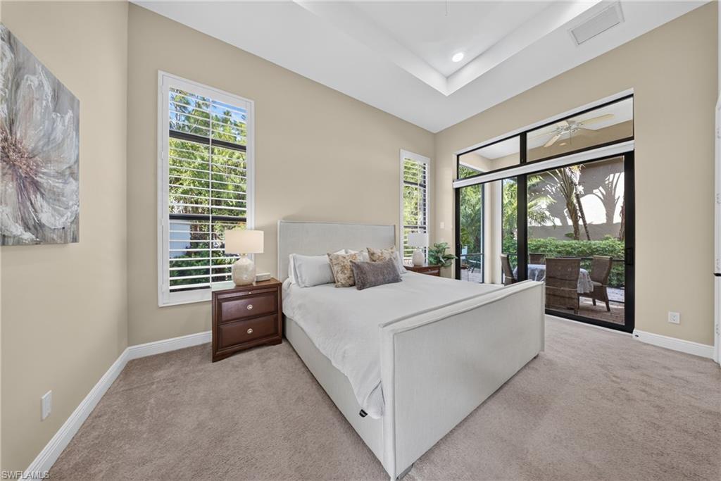 Bedroom featuring a tray ceiling with recessed lighting, plush carpet flooring, and a large sliding glass door opening to an outdoor patio