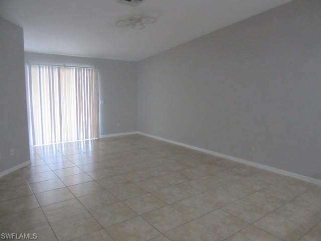 Spacious room featuring neutral tone walls, tile flooring, white baseboards, and a sliding glass door with vertical blinds