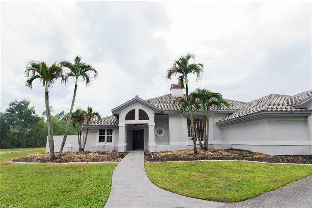 Stucco exterior with a tiled roof, arched entryway, and a paved walkway