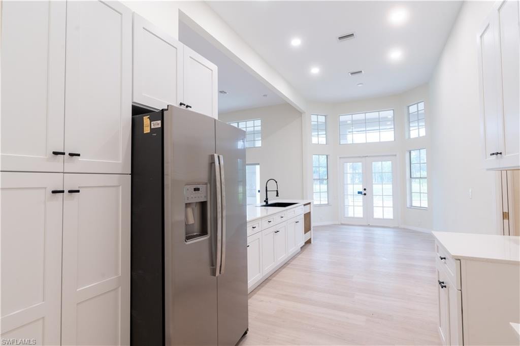 Kitchen featuring white shaker-style cabinetry, matte black hardware, stainless steel refrigerator, and wood-finish flooring