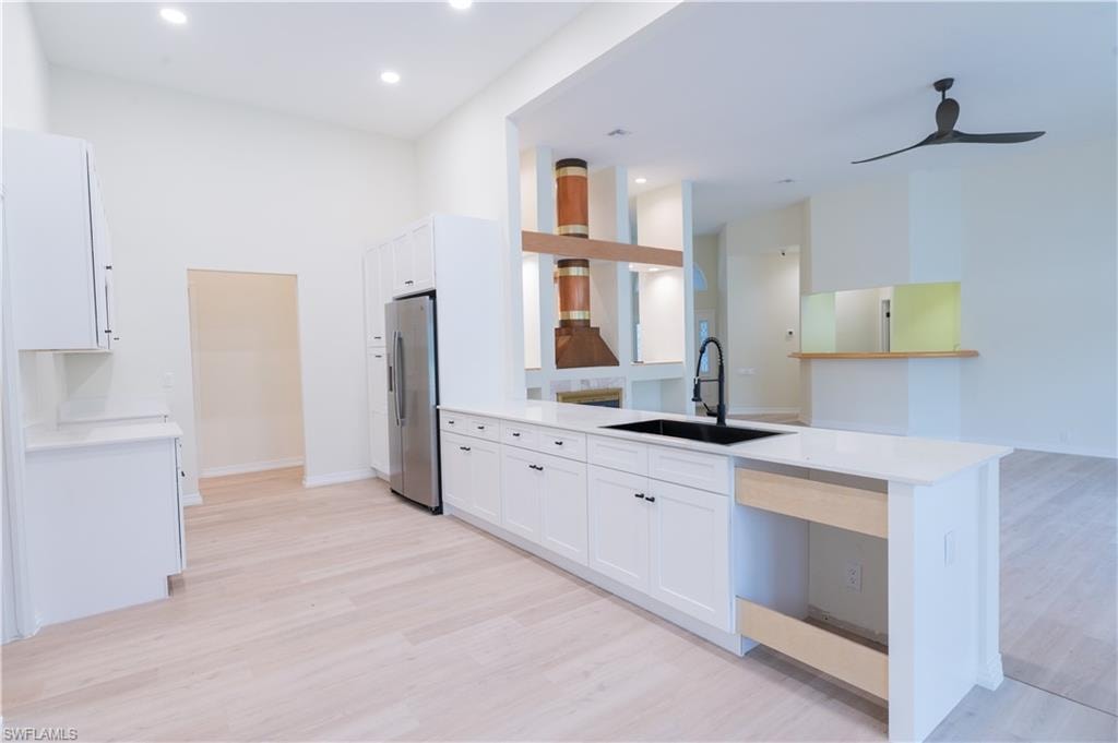 Open-concept kitchen featuring white shaker cabinetry, light wood-finish flooring, and a stainless steel refrigerator