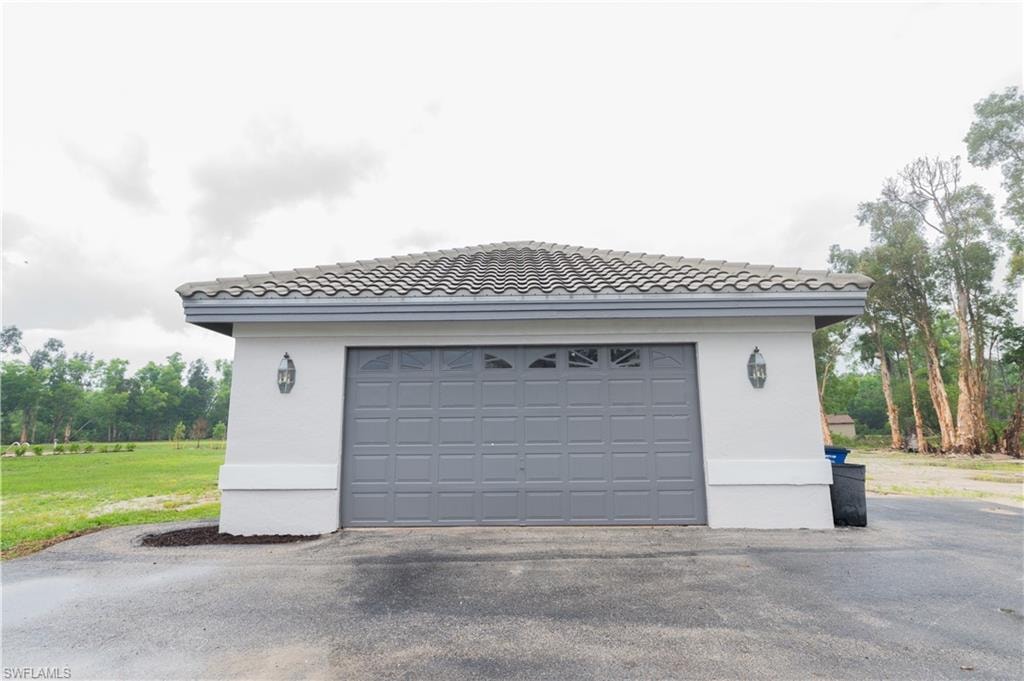 Attached garage featuring a grey paneled door with upper window inserts, white stucco exterior, and a grey tile roof