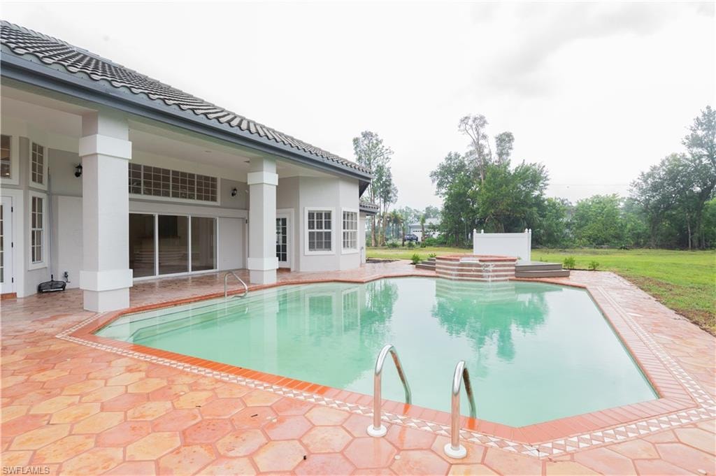 Expansive outdoor pool area featuring a geometric swimming pool with integrated spa, terracotta-style paving, and a covered patio with white columns and sliding glass doors