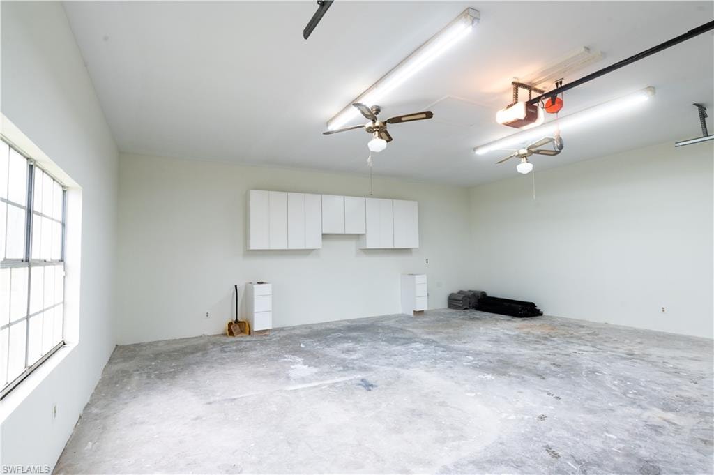 Spacious interior featuring a concrete floor, abundant overhead fluorescent lighting, multiple ceiling fans, and a large grid-pattern window