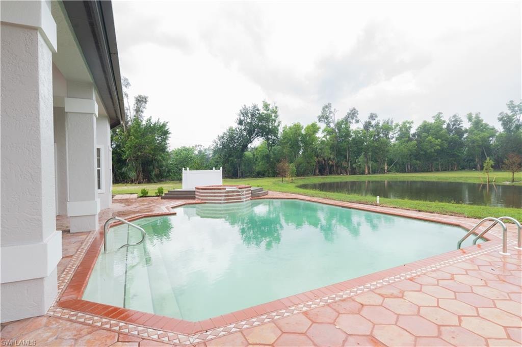 Expansive outdoor space featuring a rectangular swimming pool with steps, a raised hot tub, and a surrounding paver patio with a decorative tile border