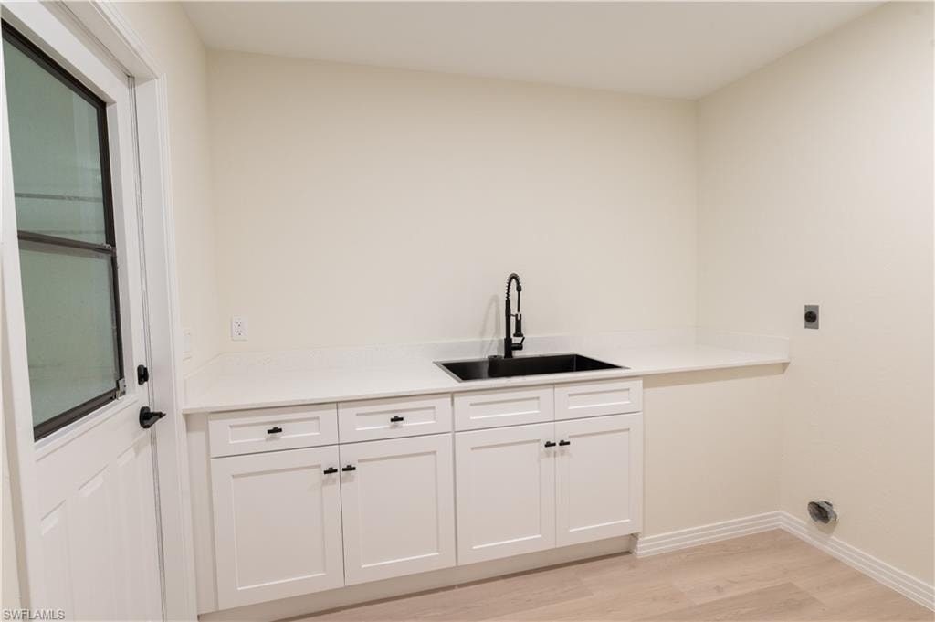 Utility room featuring white shaker cabinetry, a deep black sink with matte black faucet, light quartz-style countertops, and wood-finish flooring