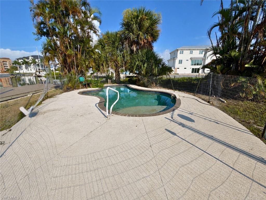 Freeform swimming pool featuring a light-colored paved deck and surrounding tropical foliage - Virtually Edited Image