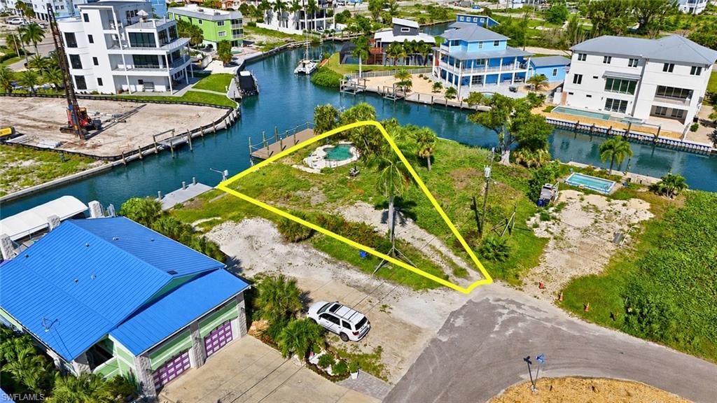 Waterfront property featuring a private boat dock, an in-ground pool, mature palm trees, direct canal access, and a paved road approach - Virtually Edited Image