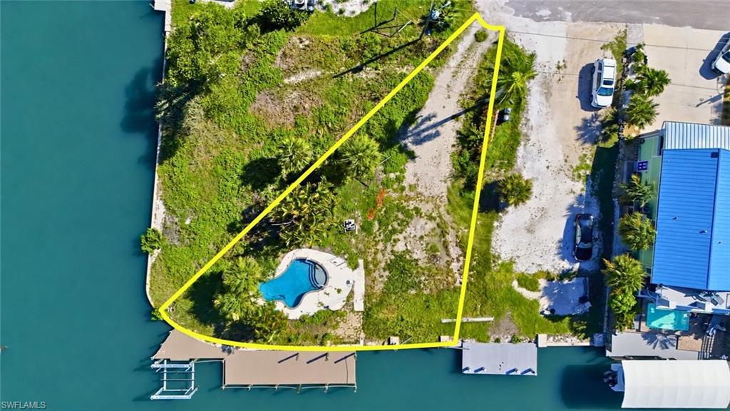 Waterfront property featuring a private pool with surrounding hardscaping, a dock structure, and ample green space - Virtually Edited Image