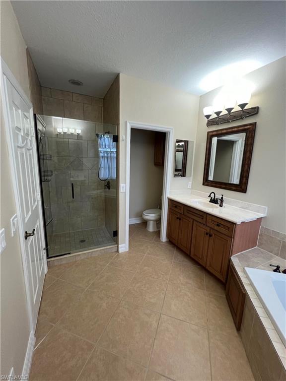 Full bathroom with tile flooring, a textured ceiling, shower with separate bathtub, vanity, and toilet