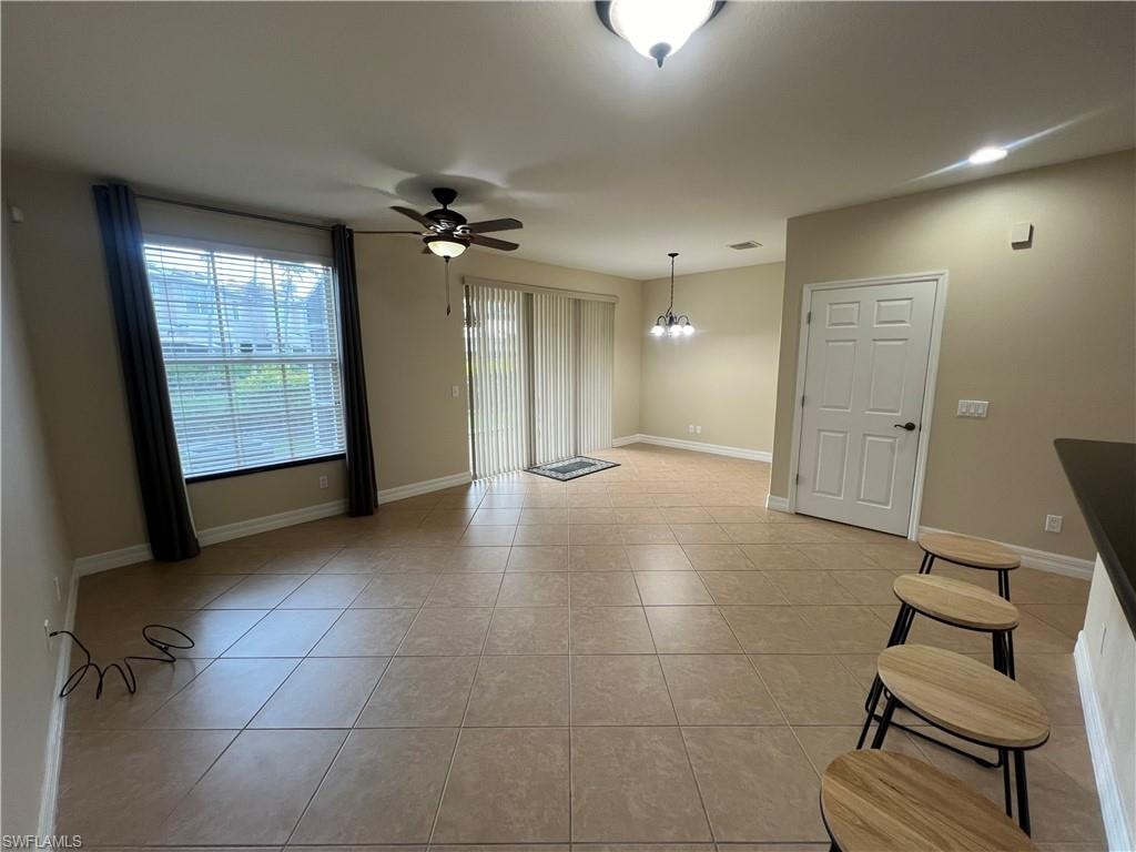 Unfurnished living room featuring light tile floors and ceiling fan with notable chandelier