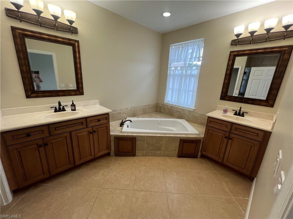 Bathroom with dual vanity, a relaxing tiled bath, and tile flooring
