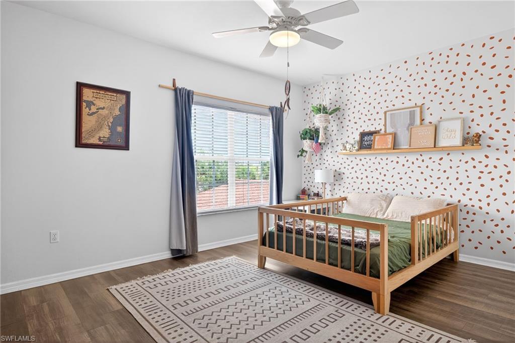 Room featuring wood-finish flooring, a ceiling fan with integrated lighting, a window with horizontal blinds, and a built-in wall shelf