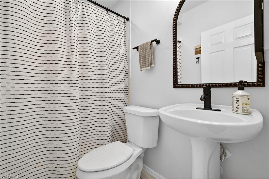 Bathroom featuring a pedestal sink with a matte black faucet, a framed mirror, and a white toilet