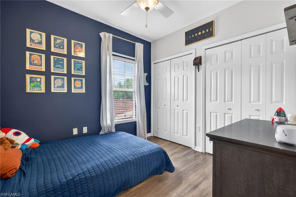Bedroom featuring wood-finish flooring, a ceiling fan, window with blinds, and white bi-fold closet doors