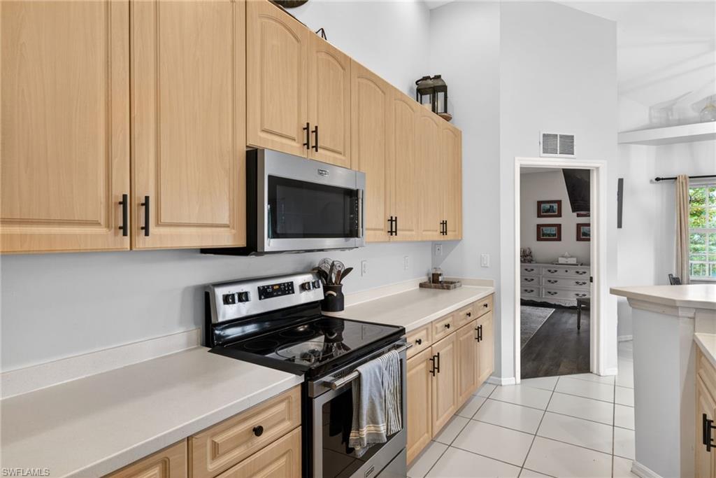 Kitchen featuring light wood-finish cabinetry with black hardware, stainless steel appliances, solid surface countertops, and tiled flooring