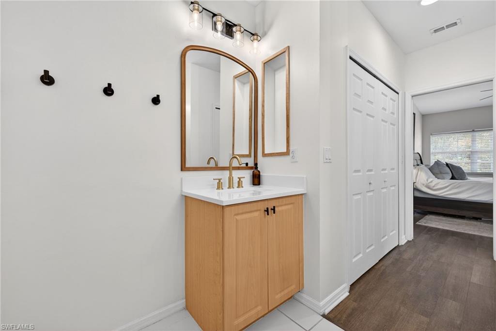 Bathroom vanity featuring a light wood-finish cabinet with black hardware, a white countertop, and a gold-finish faucet