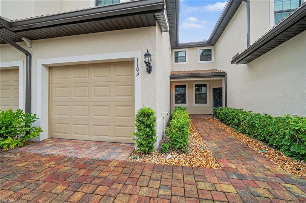 Stucco exterior with a tiled entry roof, integrated garage, and a paver driveway
