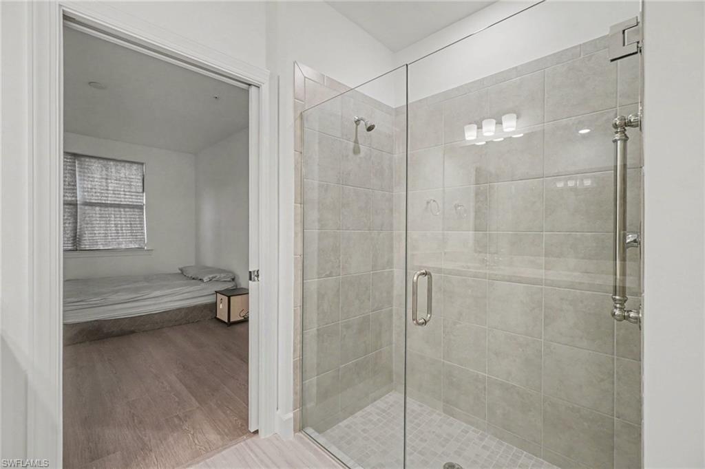 Glass-enclosed shower featuring light grey wall tiling and a tiled shower pan