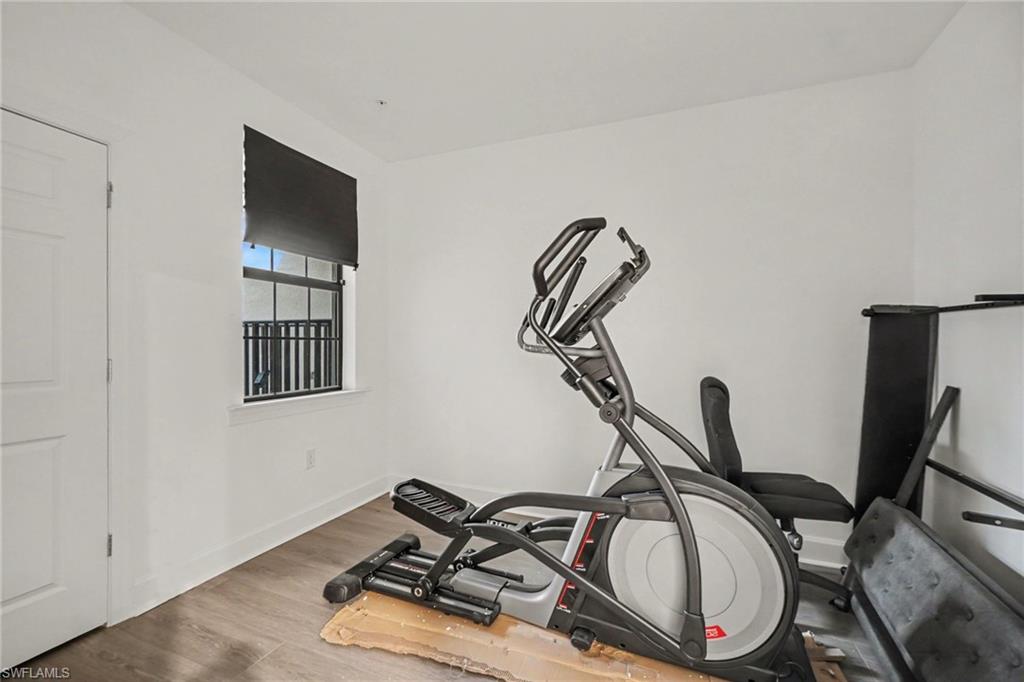 Room with wood-finish flooring, white walls, and a window featuring a dark roller shade and black metal grilles