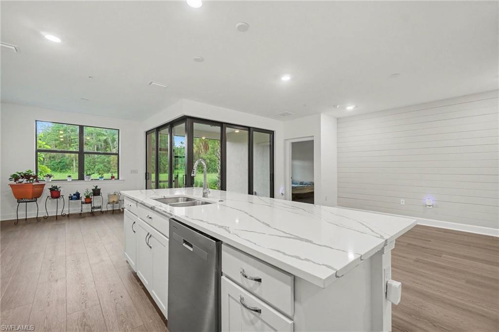Kitchen island featuring a white countertop with veining, an undermount sink with a gooseneck faucet, a built-in dishwasher, and white cabinetry