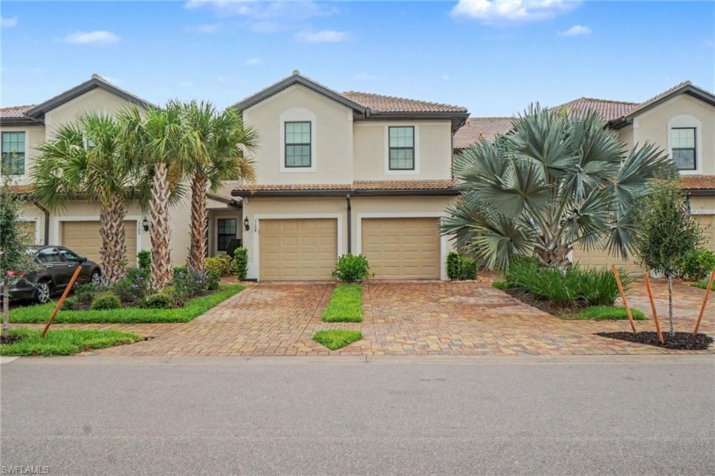 Stucco exterior with tile roofing, featuring a paver driveway, two-car garage, and mature landscaping