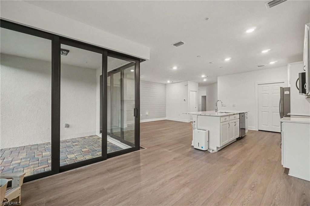 Open-concept living space with wood-finish flooring, recessed lighting, and a white kitchen island featuring a sink and a dishwasher